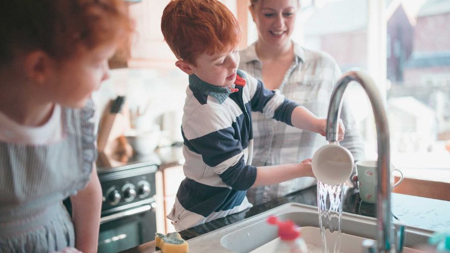 Two children washing up in the kitchen sink with their mum